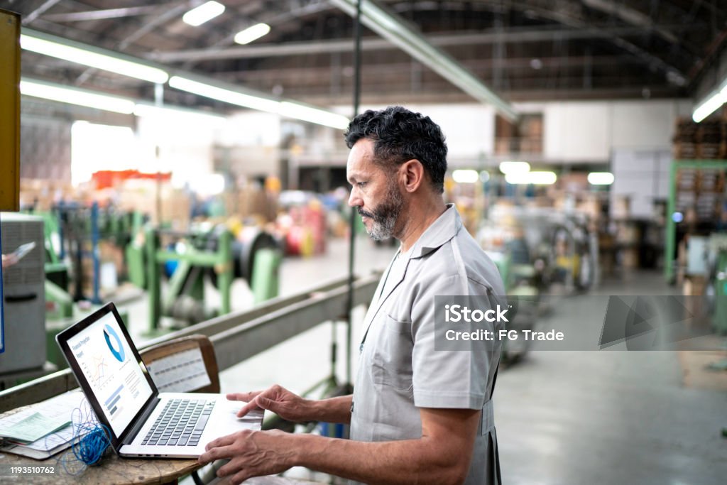 Technician using laptop while working in a factory Manufacturing Stock Photo