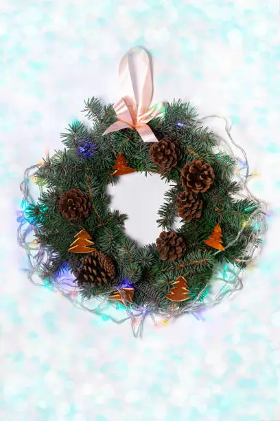 Christmas wreath flatlay. Green spruce branches decorated with orange zest, lights, pine cones and ribbon bow on white background,festive style.New Year 2020 concept.Hand made eco-friendly decorations