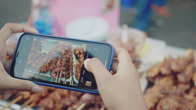 Young women taking photo of chicken and pork grill at street food