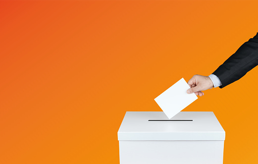 La mano de una persona usa un voto en las urnas en las elecciones. Con fondo naranja photo