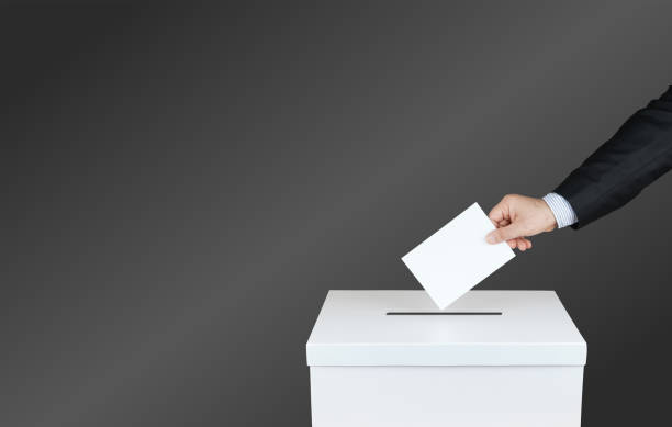 la mano de una persona usa un voto en las urnas en las elecciones. con fondo negro - urna de voto fotografías e imágenes de stock