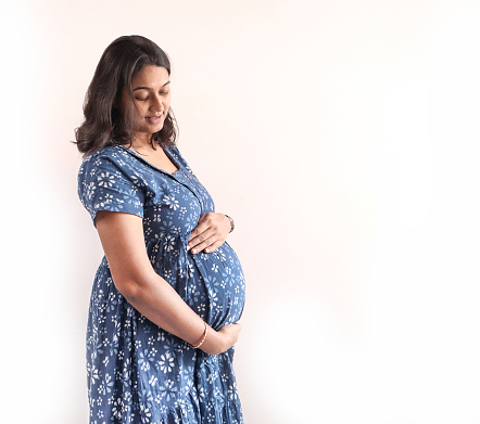 A pregnant indian lady with blue dress and hands on belly