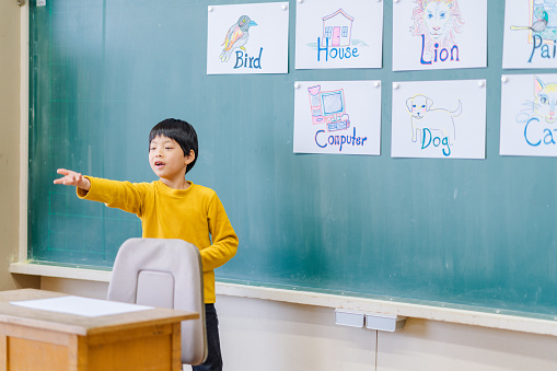 A group of male and female school children are learning English while playing games in an elementary school building classroom.