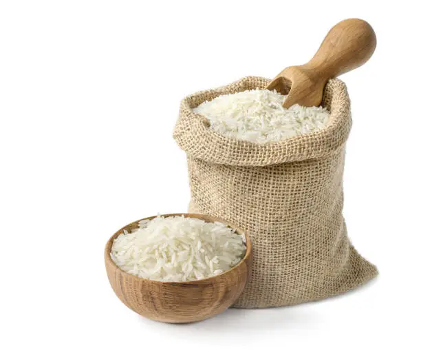 Photo of Dry white long rice basmati in wooden bowl and burlap sack with wooden scoop isolated on white background.