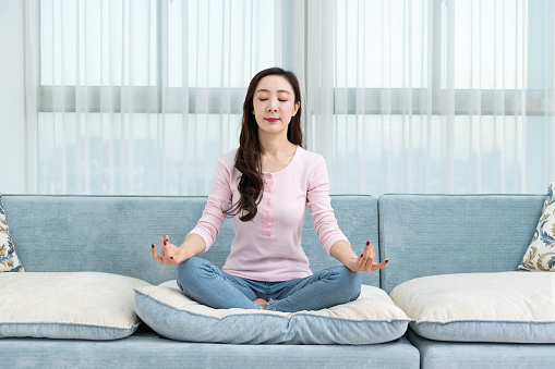 Woman sitting on sofa and doing yoga exercises.