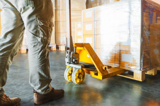 istock Warehouse worker unloading shipment goods pallet with hand pallet truck. 1193542687