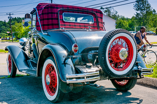 Calais, Maine, USA - July 14, 2015 : 1931 Chevrolet convertible parked near the road in rural Maine. A man rides his bicycle in the background.