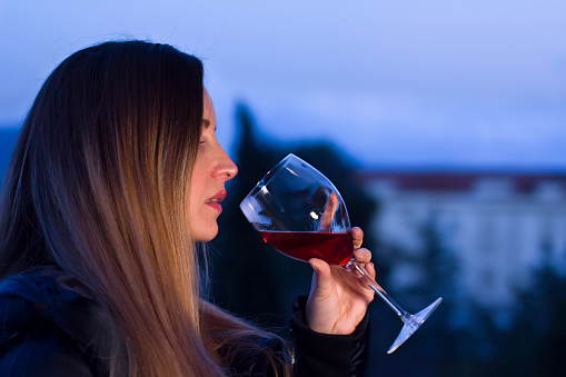 Young woman relaxing and drinking a glass of red wine at home at sunset in the evening