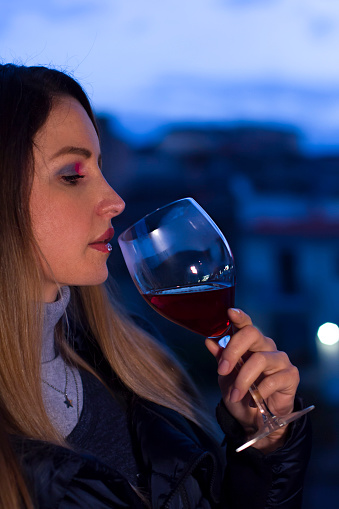 Young woman relaxing and drinking a glass of red wine at home at sunset in the evening