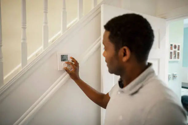 A side-view shot of an Ethiopian man turning down a thermostat in his home.