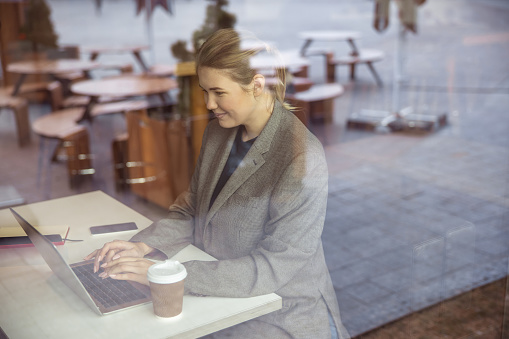 Joyful lady behind glass sitting at the table and using notebook stock photo