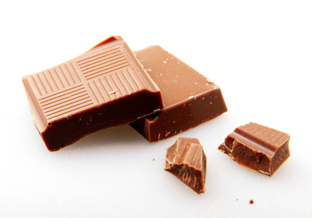 A conceptual food photograph featuring a milk chocolate bar standing on warm golden sand dunes, set against a soft, dreamy desert background. This surreal composition highlights the contrast between luxury chocolate and extreme environmental conditions, symbolizing melting, heat, and the richness of indulgence.