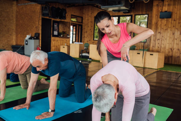 Yoga instructor helping seniors doing a cat yoga pose Group of seniors practicing yoga with the help of the young instructor. cat pose yoga stock pictures, royalty-free photos & images