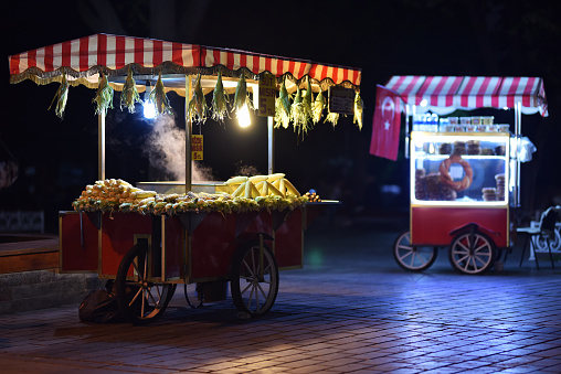 Traditional carts of Turkish street food in night. Text on signboards in translation from Turkish language on English is Roasted chestnuts and corn.