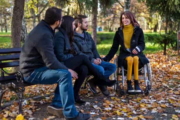 Disabled young woman in a wheelchair enjoying with friends in the park stock photo