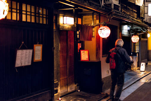 Kyoto, Japan - April 9, 2019: Gion area in dark evening night and people walking by izakaya restaurant entrance and hanging paper lanterns