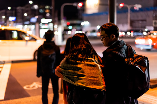 Kyoto, Japan - April 9, 2019: Closeup of young couple people waiting to cross street in Gion district at dark evening night with traffic cars and bokeh blurry background
