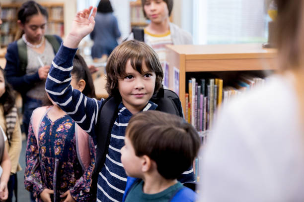 istock Elementary age boy raises hand to ask unrecognizable teacher question 1193583435