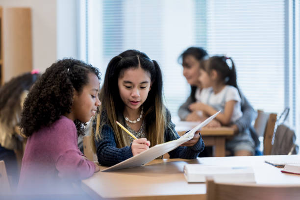 istock Cute schoolgirl helps her friend study for a test 1193583660