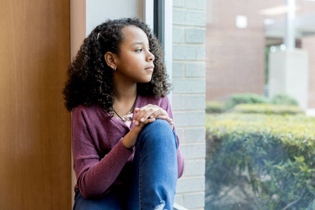 Lonely preteen schoolgirl Lonely mixed race preteen schoolgirl day dreams as she looks through the window while at school. critical thinking kids stock pictures, royalty-free photos & images