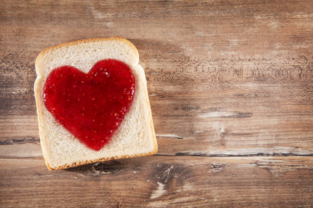 slice of bread and heart shaped jam on rustic wooden table - raspberry heart shape gelatin dessert valentines day imagens e fotografias de stock