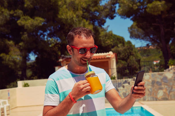 istock Attractive man using cellphone while drinking juice near swimming pool. 1193586204