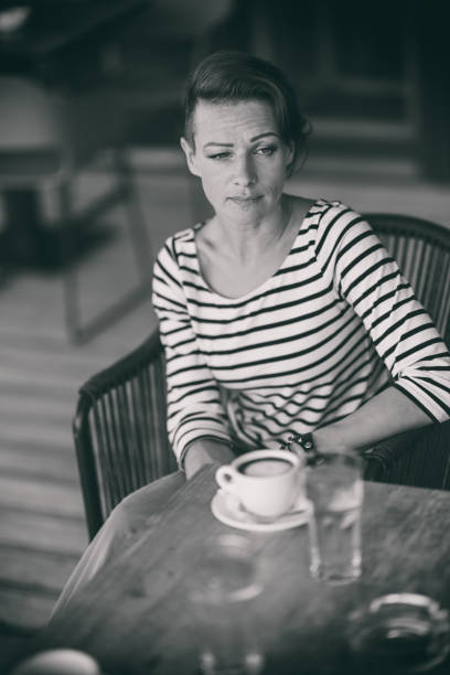 Black and white photo of mature woman wearing stripe shirt sitting alone in the cafe