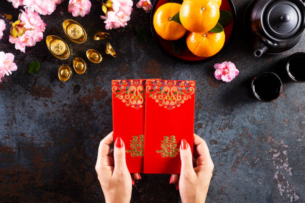 Chinese new year festival decorations. Woman hand holding pow or red packet, orange and gold ingots on a black stone texture background. Chinese characters FU means fortune good luck, wealth, money flow. decoraciones de festivales de año nuevo chino. mujer mano sosteniendo pow o paquete rojo, ingotes naranjas y dorados sobre un fondo de textura de piedra negra. caracteres chinos fu significa fortuna buena suerte, riqueza, flujo de dinero.