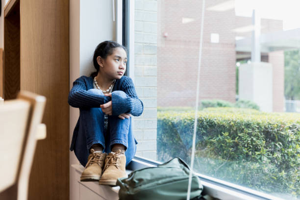 istock Feeling left out, middle school girl looks out window 1193589518