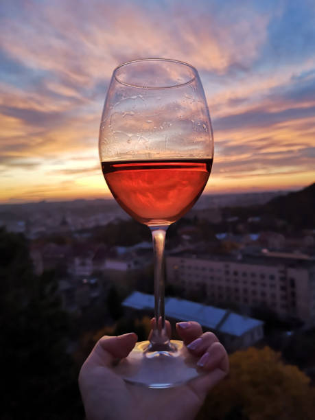 Wine swirl with a sky and sunset. Wineglass with woman hand swirling rose red drink outdoor during harwest or wine tasting
