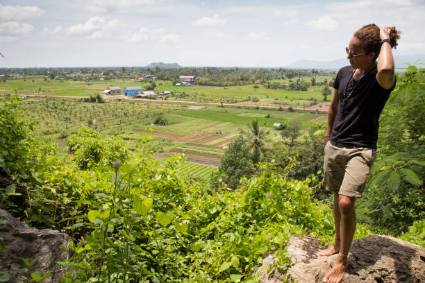 Male tourist looking at green rice paddy fields from high angle, Cambodia