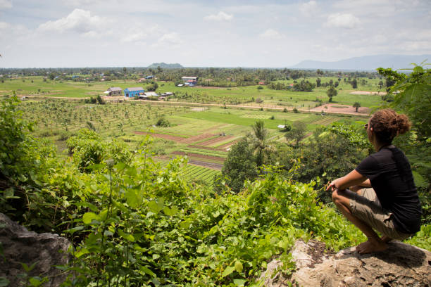 One young man with curly hair, wearing shorts and a black shirt, looking at the green rice paddy fields of Cambodia