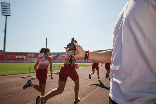Young athletics team on a sports stadium, exercising together, being overlooked by a coach.