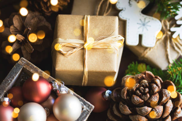 istock Christmas and New Year gift boxes wrapped in brown paper pine cones tree decorations baubles in wood box in golden sparkling lights 1193603668