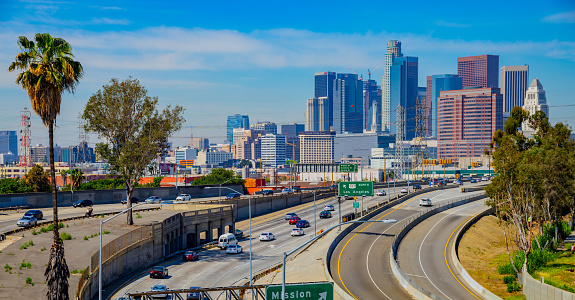 Freeway with traffic in the foreground leading back to the skyscrapers of Los Angeles skyline with thin clouds above, California