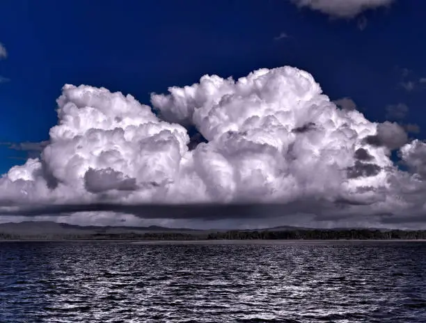 A spectacular dramatic brightly coloured cloudy sea water tropical seascape featuring awesome billowing white Cumulus cloud formation in a dark blue sky with ocean water reflections. Australia.