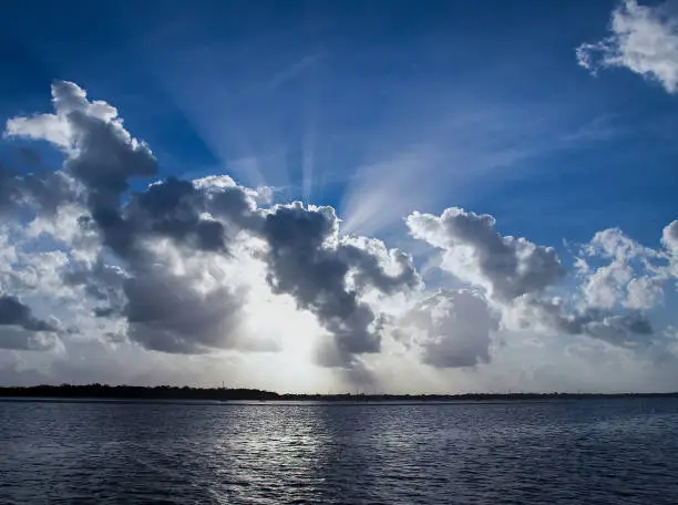 A spectacular inspirational brightly coloured cloudy sea water tropical seascape featuring a billowing white Cumulus cloud formation and clear Crepuscular Rays in a mid blue sky with ocean water reflections, Australia.