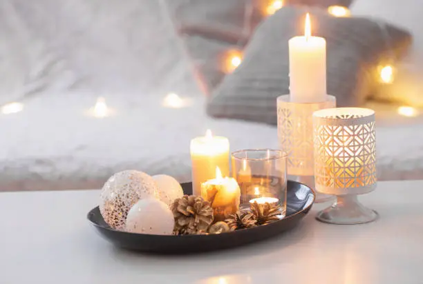 Christmas decoration   with burning candles on  white table against the background of  sofa with plaids and pillows. Cozy home and holiday concept