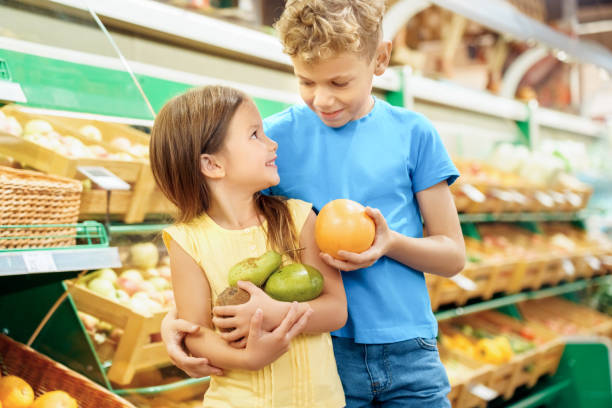 果物を手にスーパーマーケットに立つ子供たち - two pears ストックフォトと画像