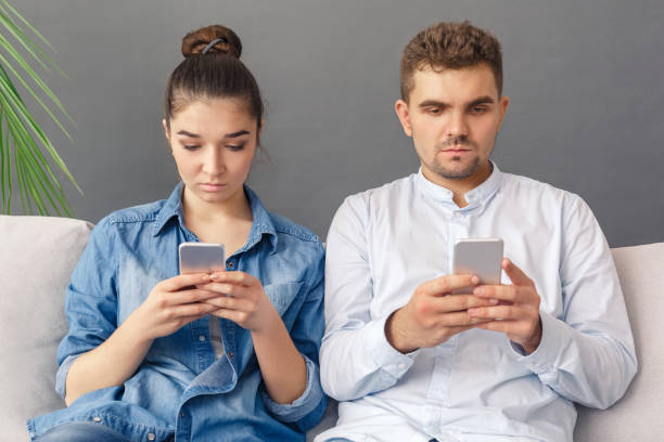 istock Modern Relationnship Concept. Young couple sitting on sofa studio isolated on grey browsing smartphone concentrated 1193614282