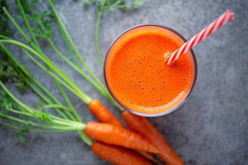 Overhead view of fresh organic carrot juice with a striped drinking straw