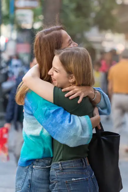 Photo of Happy mother and teenage daugher hugging each other on the steet.