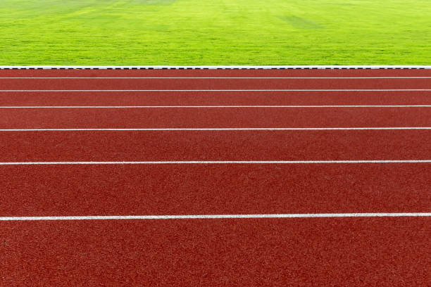 istock Red treadmill and white line at the stadium with green grass. 1193643145