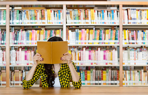 Woman hiding behind a book in library.