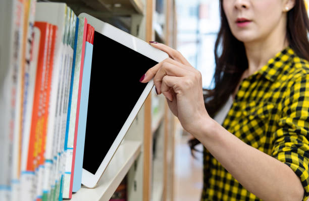 本棚からデジタルタブレットを選ぶ女性 - bookstore student chinese ethnicity book ストックフォトと画像