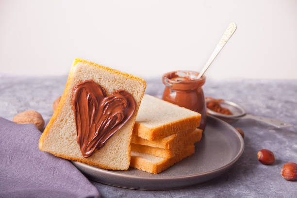 Bread toast with heart shaped chocolate cream butter, jar of chocolate cream on the concrete background