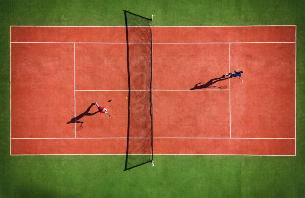 Drone view of tennis match from above with player's shadow Drone view of tennis match from above with player's shadow sports court photos stock pictures, royalty-free photos & images