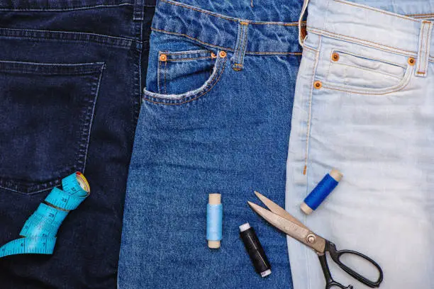 Three pair of jeans with scissors, threads and tailor meter. Upcycle concept.