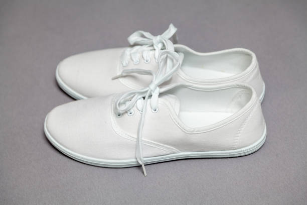 Two new white sneakers with laces stand on a gray isolated background. Laces tied in a common knot