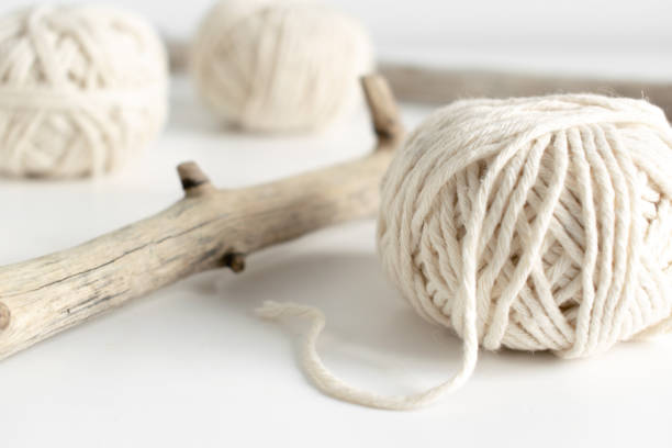 Balls of white yarn and rustic sticks on a white table. Threads of wool boho image.Good for macrame and handicrafts banners and advertisement stock photo